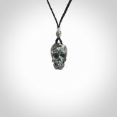 This picture shows a small sized Zebra Marble stone skull pendant that we have hand carved. It is polished to a soft shine and is a very striking piece. The cord is black and has a small grey floret binding just above the pendant.